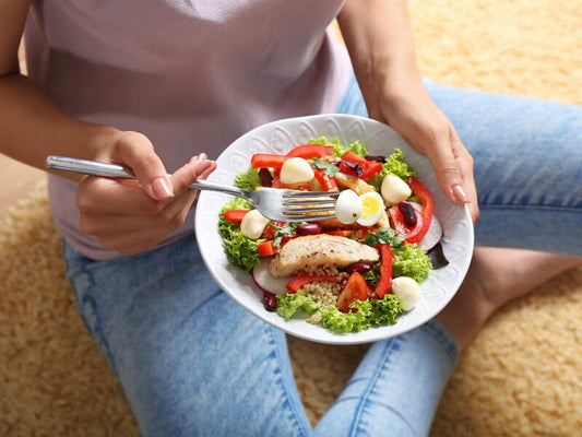 A girl sitting on the ground eating a salad