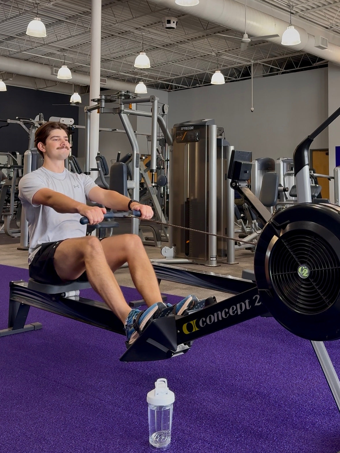 Person using a rowing machine in a gym with a bottle of water on the floor.